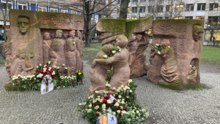 Foto des Block der Frauen nach einer Gedenkveranstaltung. Die Statuen sind mit weißen Rosen und Gedenkkränzen geschmückt.