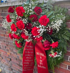 Foto des Gedenkkranzes an der Levetzowstraße. Er besteht aus roten Rosen, kleinen weißen Blüten und grünem Gesteck. Auf der Schärpe steht ein Zitat von Esther Bejarano „Ihr tragt keine Schuld für das was passiert ist, aber ihr macht euch schuldig, wenn es euch nicht interessiert“ mit dem sie sich an Deutsche Nachkommen gerichtet hat. Auf der anderen Seite des Bandes steht „DIE LINKE. In der BVV Berlin Mitte“.