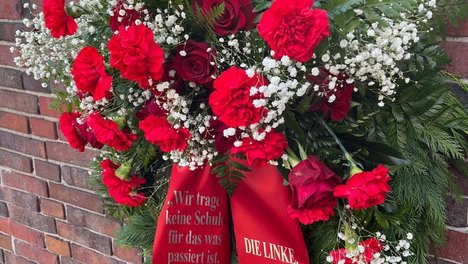 Foto des Gedenkkranzes an der Levetzowstraße. Er besteht aus roten Rosen, kleinen weißen Blüten und grünem Gesteck. Auf der Schärpe steht ein Zitat von Esther Bejarano „Ihr tragt keine Schuld für das was passiert ist, aber ihr macht euch schuldig, wenn es euch nicht interessiert“ mit dem sie sich an Deutsche Nachkommen gerichtet hat. Auf der anderen Seite des Bandes steht „DIE LINKE. In der BVV Berlin Mitte“.
