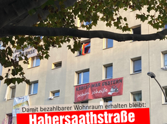 Foto von der Habersaathstraße 40-48. Auf einem Banner unterm Fenster steht „Abriss war gester scho scheiße“. In einer Textbox darunter steht: „Damit bezahlbarer Wohnraum erhalten bleibt: Habersaathstraße Rekommunalisieren!“