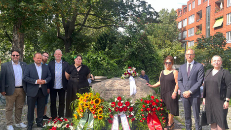 Mitglieder der BVV Mitte stehen am Gedenkstein für die Maueropfer an dem viele Blumenkränze gelehnt sind. Zu sehen ist unter anderem unsere Bezirksverordnete Deniz Seyhun.