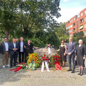 Mitglieder der BVV Mitte stehen am Gedenkstein für die Maueropfer an dem viele Blumenkränze gelehnt sind. Zu sehen ist unter anderem unsere Bezirksverordnete Deniz Seyhun.