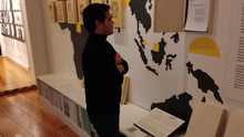 Foto des Bezirksverordneten Samiullah Haidary beim Besuch des Museums der Trostfrauen. Er liest einen Ausstellungstext. Im Hintergrund ist ein Teil der Ausstellung sichtbar – Bleistiftportraits auf Holz die an einer Wand mit einer Weltkarte angebracht sind.