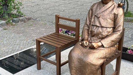Ein Foto der Friedensstatue für die Trostfauen in Berlin-Moabit. Dort steht weiß auf rot: „Die Friedensstatue bleibt!“