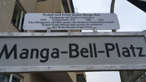 Bildmontage der neuen Straßenschilder. Oben ist das Schild des Manga-Bell-Platz zu sehen. Im angebrachten Erklärschild steht „Rudolf und Emily Duala Manga Bell. Königspaar der Duala in Kamerun. Rudolf wurde 1873 geboren und 1914 higerichtet, Emily Duala Manga Bell lebte von 1881 bis 1936. Das Königspaar kämpfte gegen die deutsche Kolonialherrschafft. Rudolf Duala Manga Bell wurde als Anführer des Widerstandes hingerichtet.  Auf dem unteren Bild ist das neue Schild der Corneilus-Fredericks-Straße zu sehen.  Im angebrachten Erklärschild steht: „Corelius Fredericks. Antikolonialer Freiheitskämpfer 1864 – 1907. Cornelius Fredericks war antikolonialer Freiheitskämpfer im damaligen Deutsch-Südwestafrike, dem heutigen Namibia. 