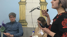 Foto vom Fastenbrechen beim „Haus der Weisheit“. Vorne rechts ist Jacky Sanehy während sie in ein Mikrofon spricht zu sehen. Sie ist Bezirksverordnete für die Fraktion DIE LINKE. in der BVV Mitte. Im Hintergrund ist die Festtafel sichtbar und zwei Menschen, deren Gesichter unkenntlich gemacht wurden. 