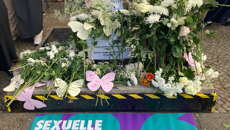 Ein Foto der Friedensstatue Ari in Berlin Moabit am 19. Juni. Sie ist bedeckt mit weiten Rosen und Zetteln mit Wünschen für die Zukunft. Auf einem Banner zu ihren Füßen steht: „Sexuelle Verbrechen kennen keine Verjährung! 19.6. Welttag zur Beseitigung sexueller Gewalt in Konflikten“