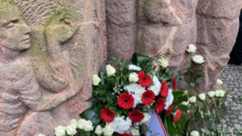 Foto vom Block der Frauen in der Rosenstraße. Angelehnt an die Statuen sind ein Gedenkkranz und weiße Rosen.