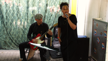 Foto vom Auftritt der Band Key of Life Pocket Soul Band. Eine Person singt in ein Mikrofon, links davon sitzt jemand und bedient ein elektronisches Schlagzeug Paddle während er auf einer elektrischen Gitarre spielt. 